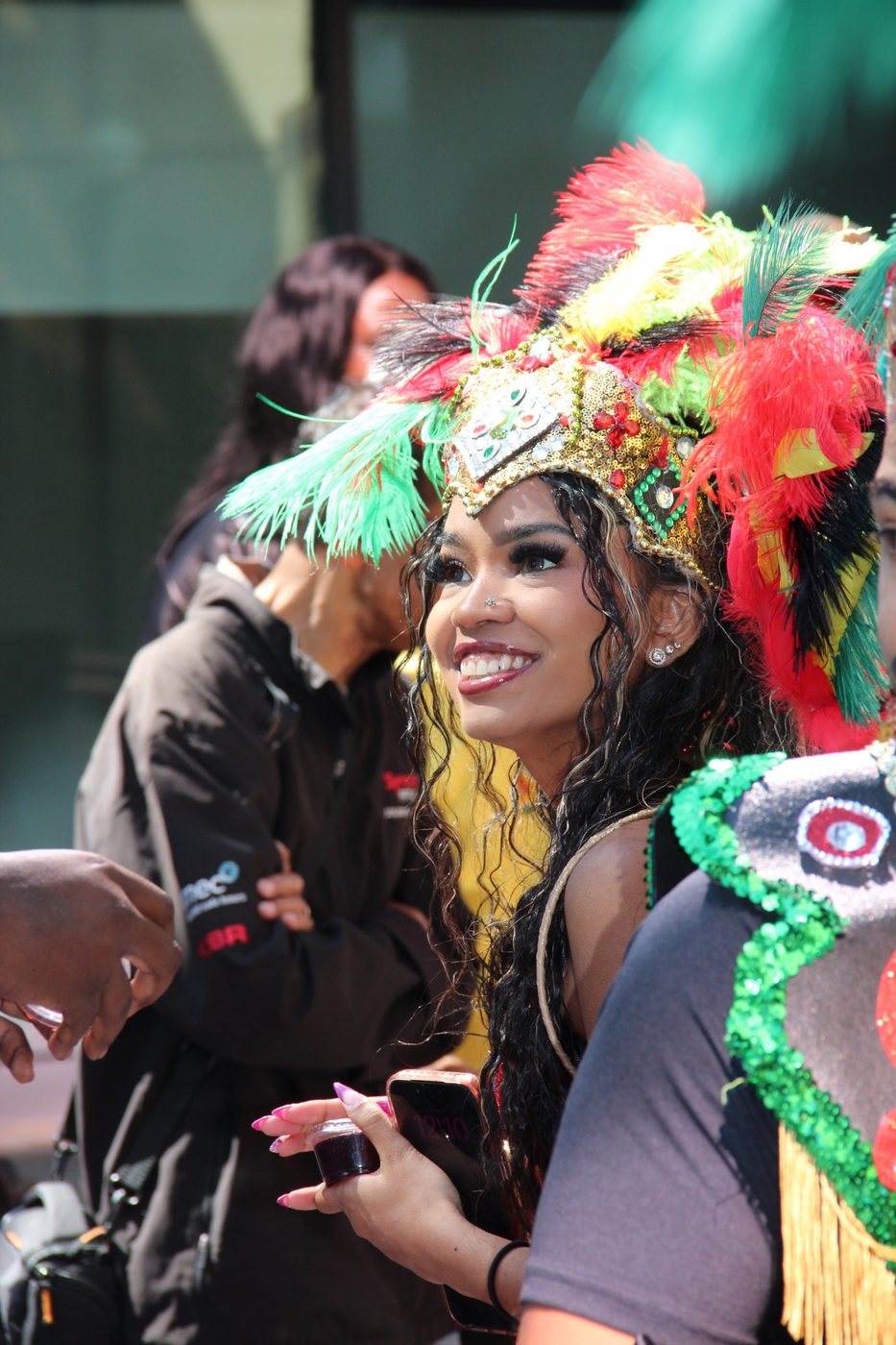 A masquerader in a green and red feathered headdress on the parade route